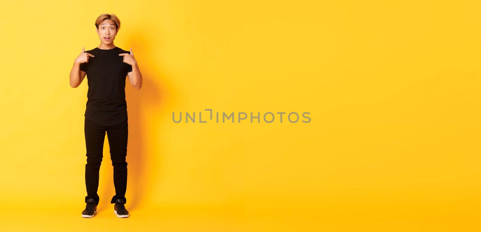 Full-length of surprised attractive korean blond guy in black outfit pointing at himself impressed, yellow background by Benzoix