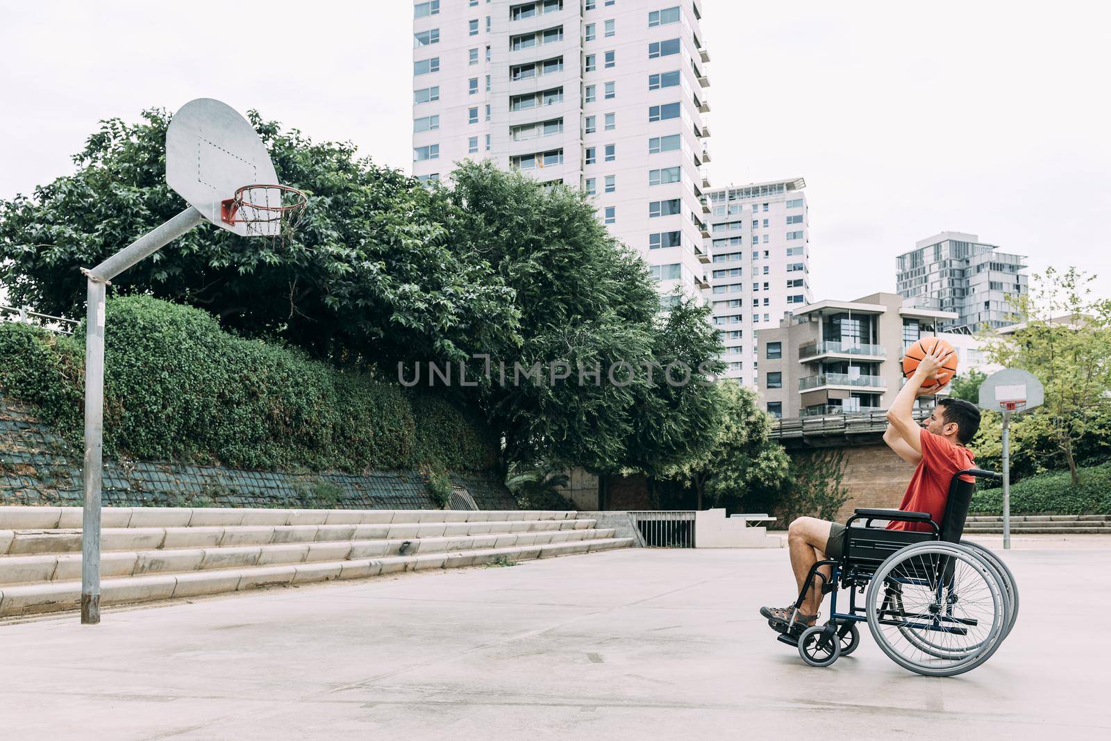 handicapped man in wheelchair throwing ball to basket alone, concept of adaptive sports and physical activity, rehabilitation for people with physical disabilities