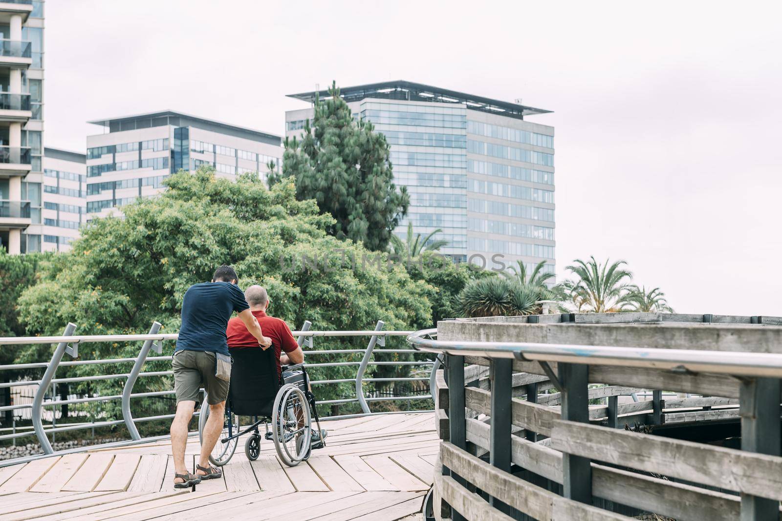 man pushes his disabled friend's wheelchair into the city, concept of friendship and integration of people with disabilities and reduced mobility problems