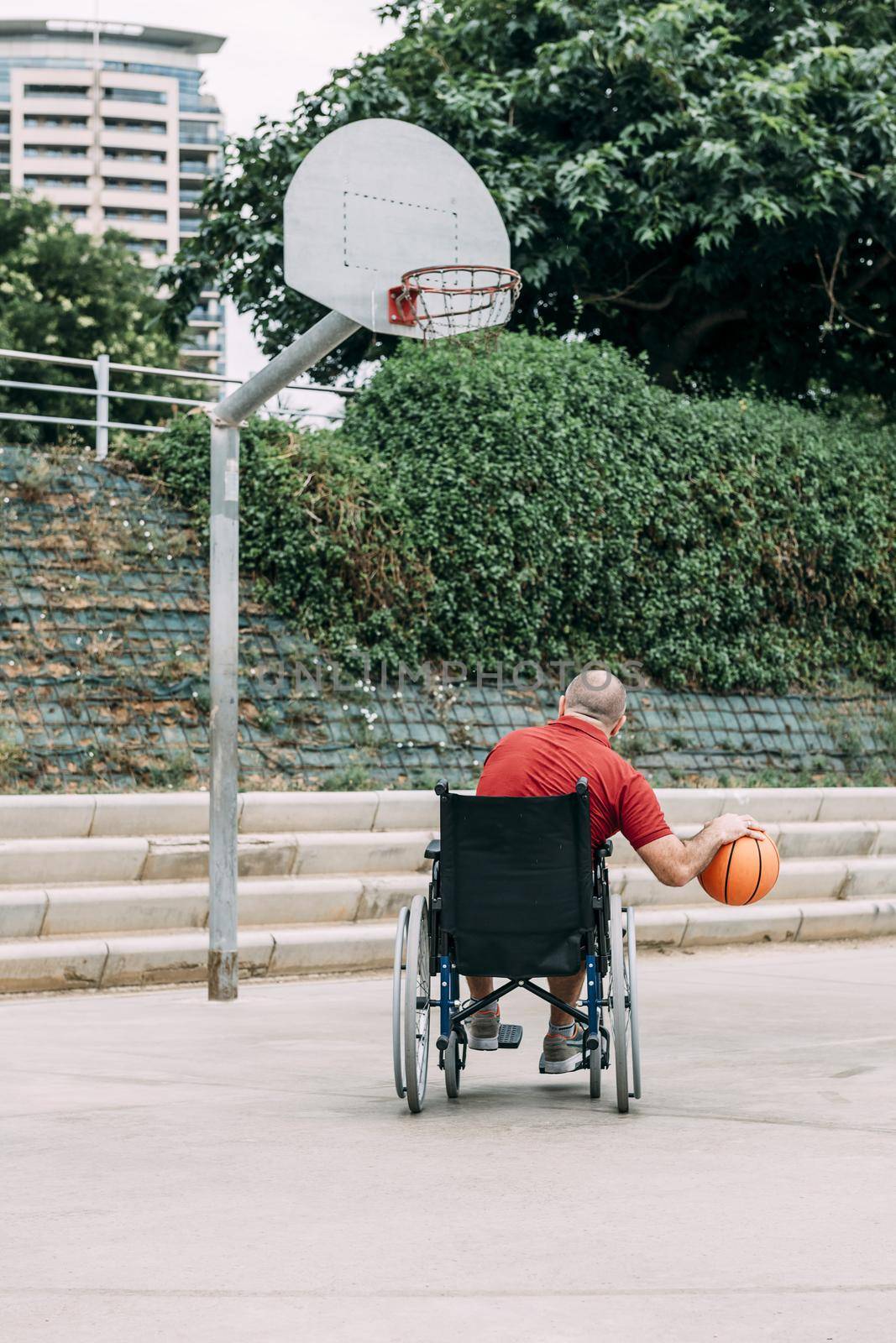 man in wheelchair playing basketball alone in the city, concept of adaptive sports and physical activity, rehabilitation for people with physical disabilities, vertical photo