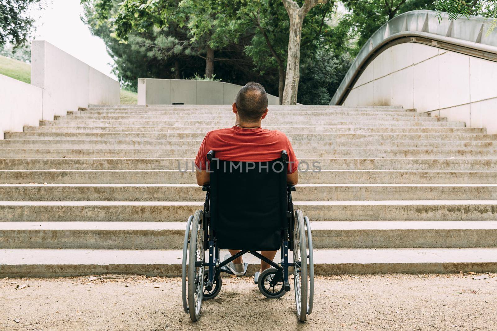 disabled man on wheelchair stopped in front of stairs who can't climb looking up for help, raising awareness of accessibility issues for people with reduced mobility