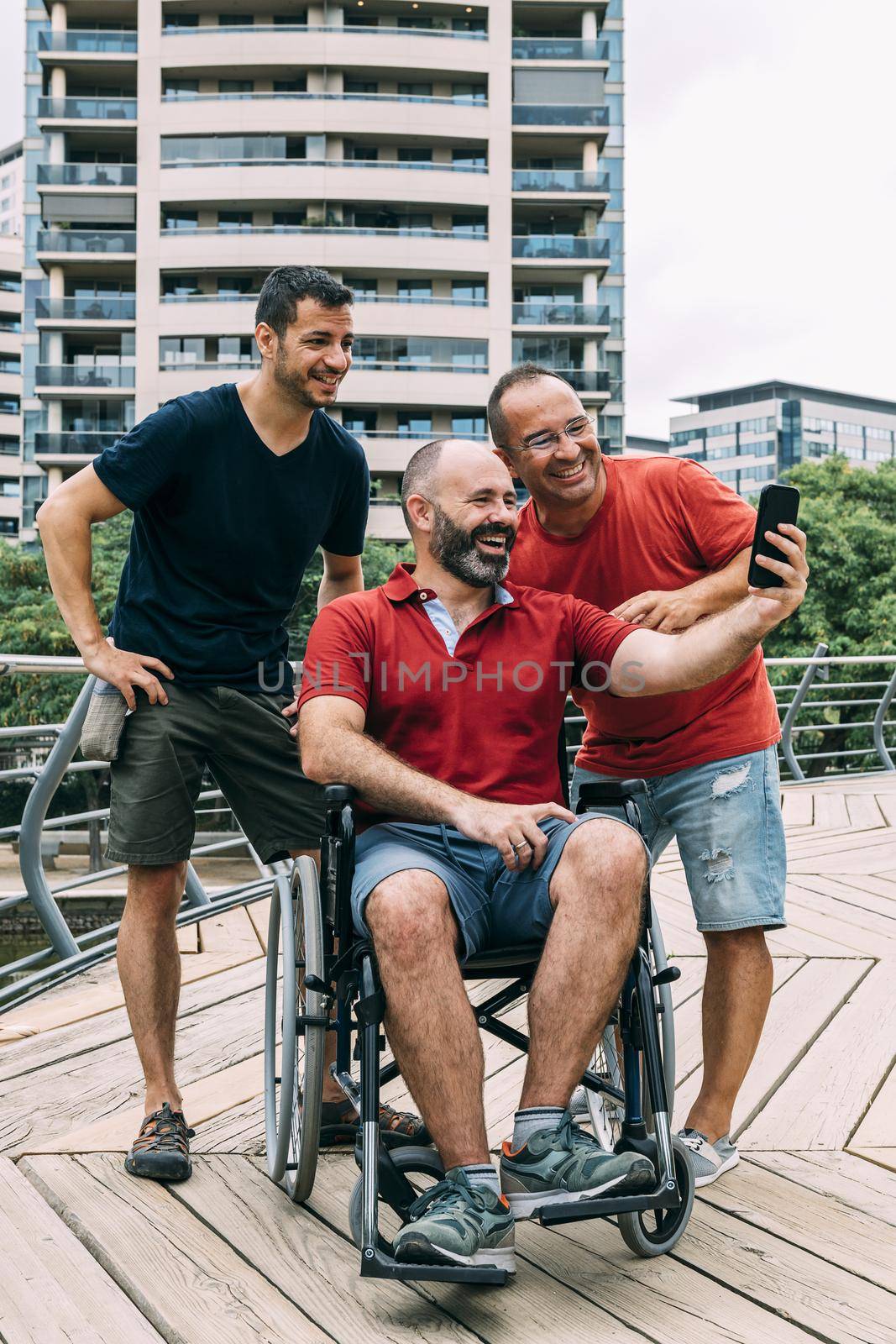 disabled man in wheelchair making selfie with his phone with two friends during a walk, concept of friendship and integration of people with disabilities and reduced mobility problems, vertical photo