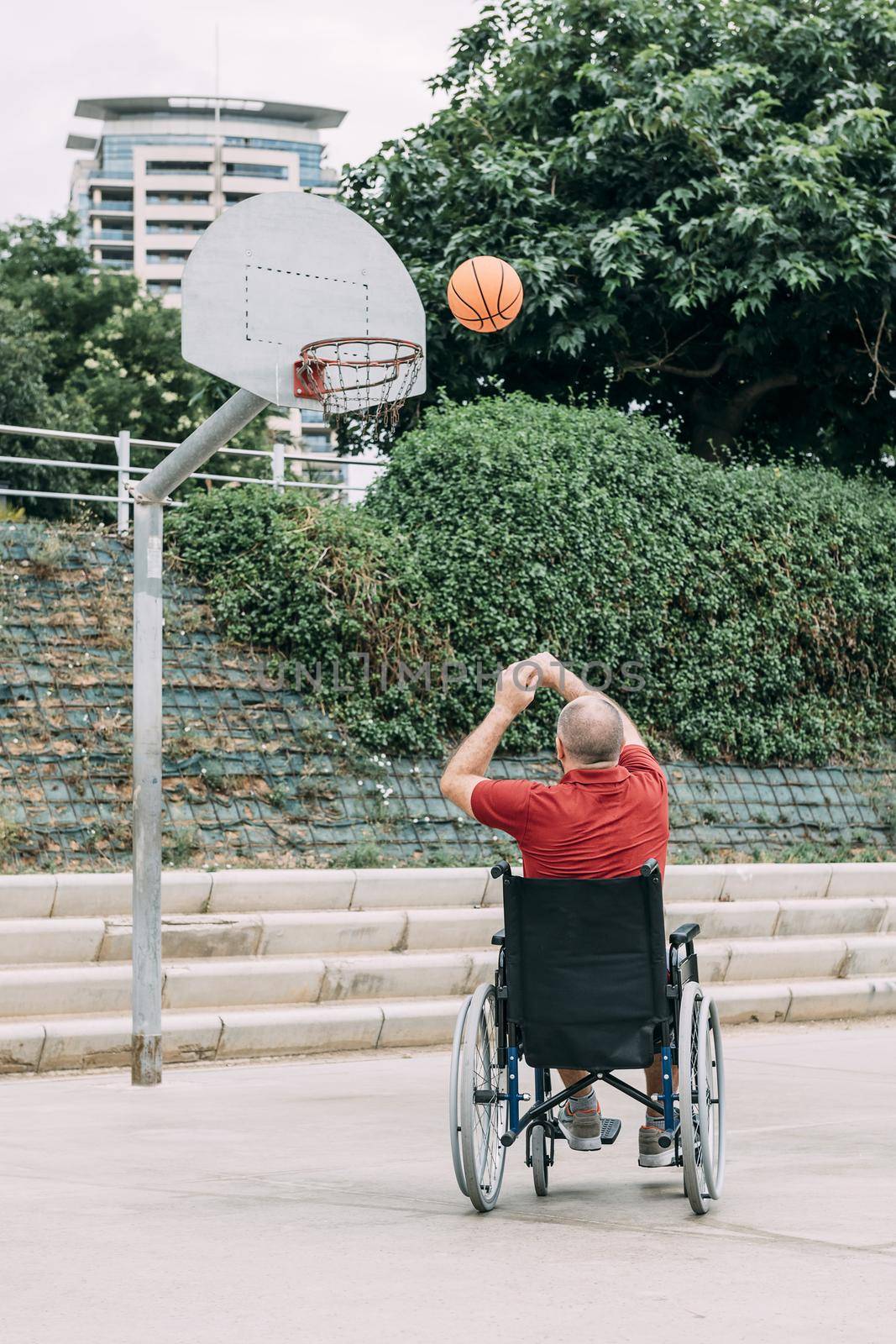 handicapped man in wheelchair playing basketball alone in the city, concept of adaptive sports and physical activity, rehabilitation for people with physical disabilities, vertical photo