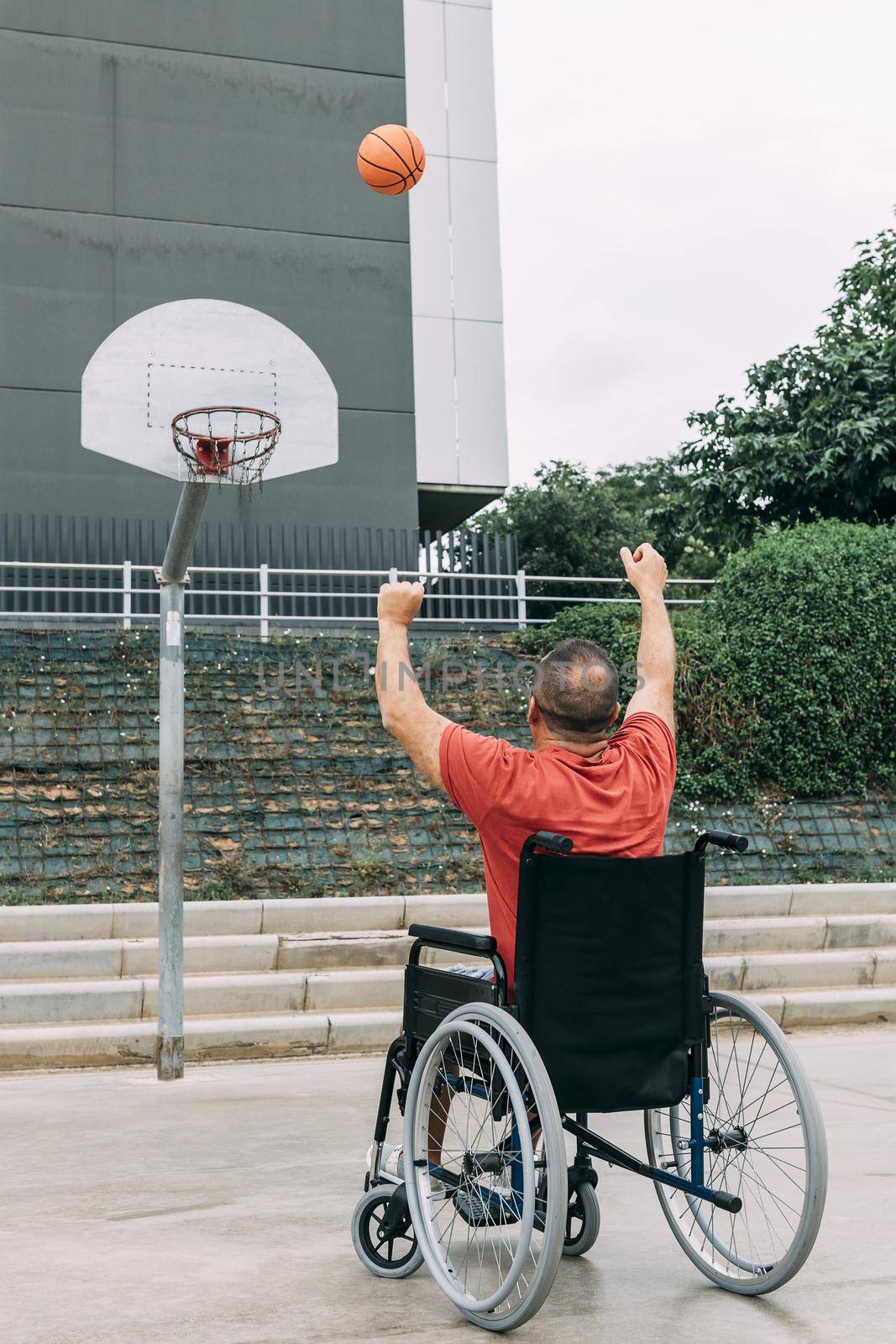 disabled man in wheelchair playing basketball alone in the city, concept of adaptive sports and physical activity, rehabilitation for people with physical disabilities, vertical photo