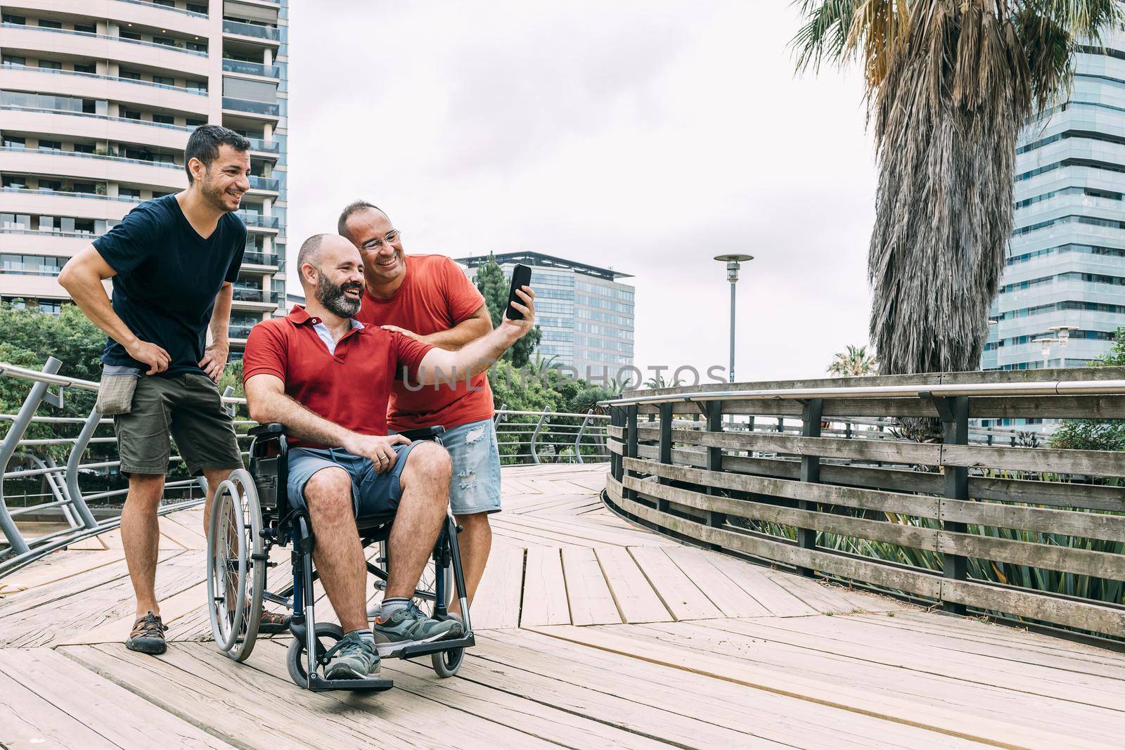 disabled man in wheelchair taking a selfie with his phone with two friends during a walk, concept of friendship and integration of people with disabilities and reduced mobility problems