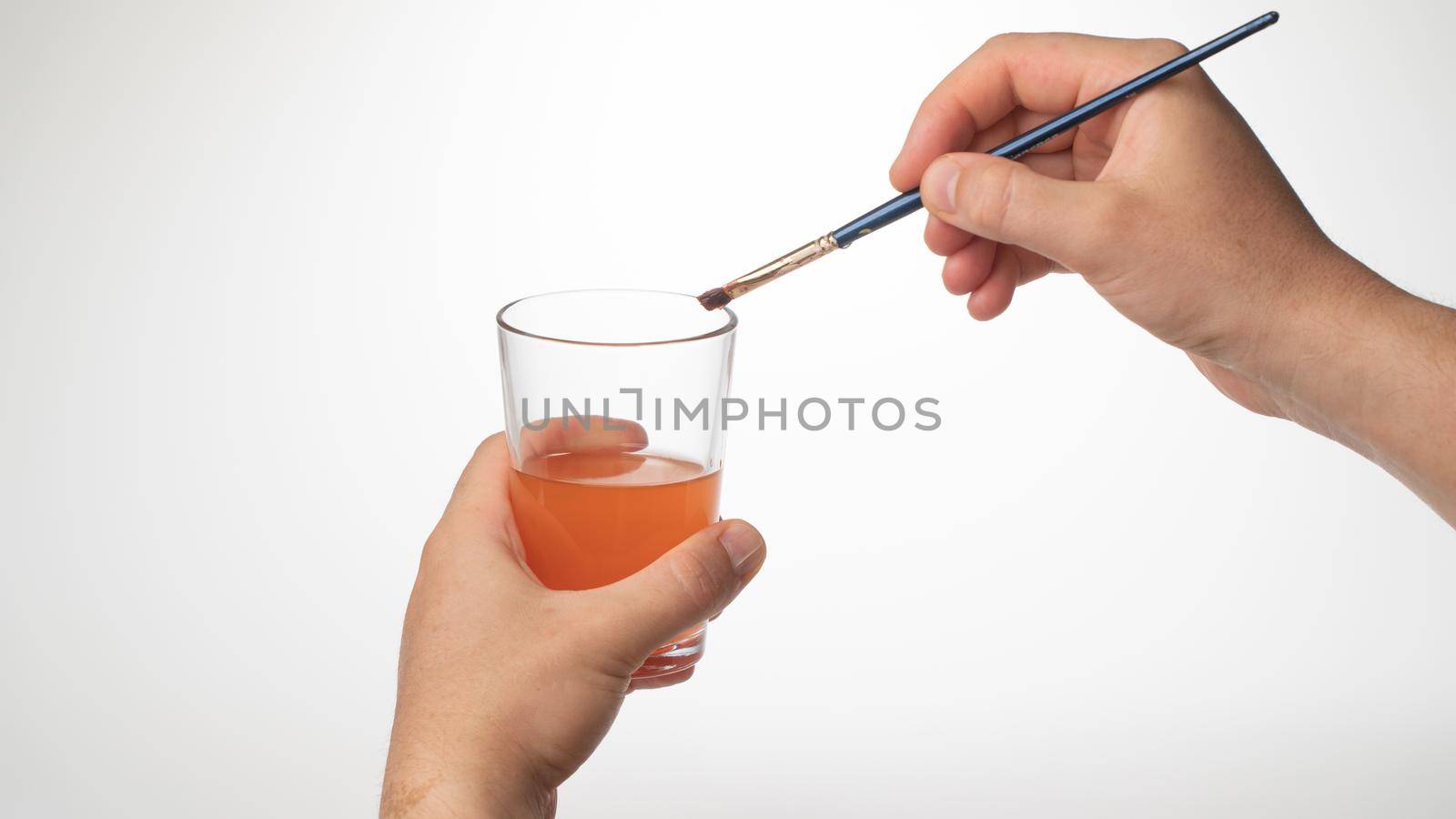 men's hand cleans the brush from the paint in a glass of water