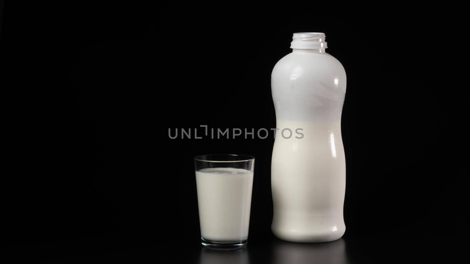 A glass of milk next to the bottle on a black background by voktybre