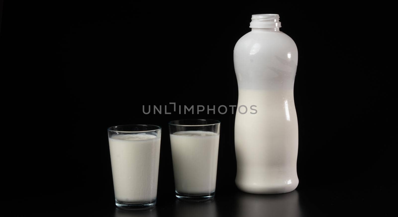 Glass with milk or kefir on a black background with a white bottle by voktybre