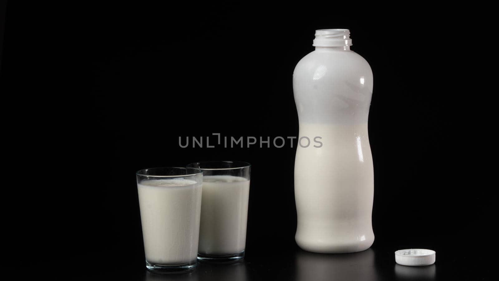 A bottle of kefir or milk with two filled glasses on a black background. High quality photo