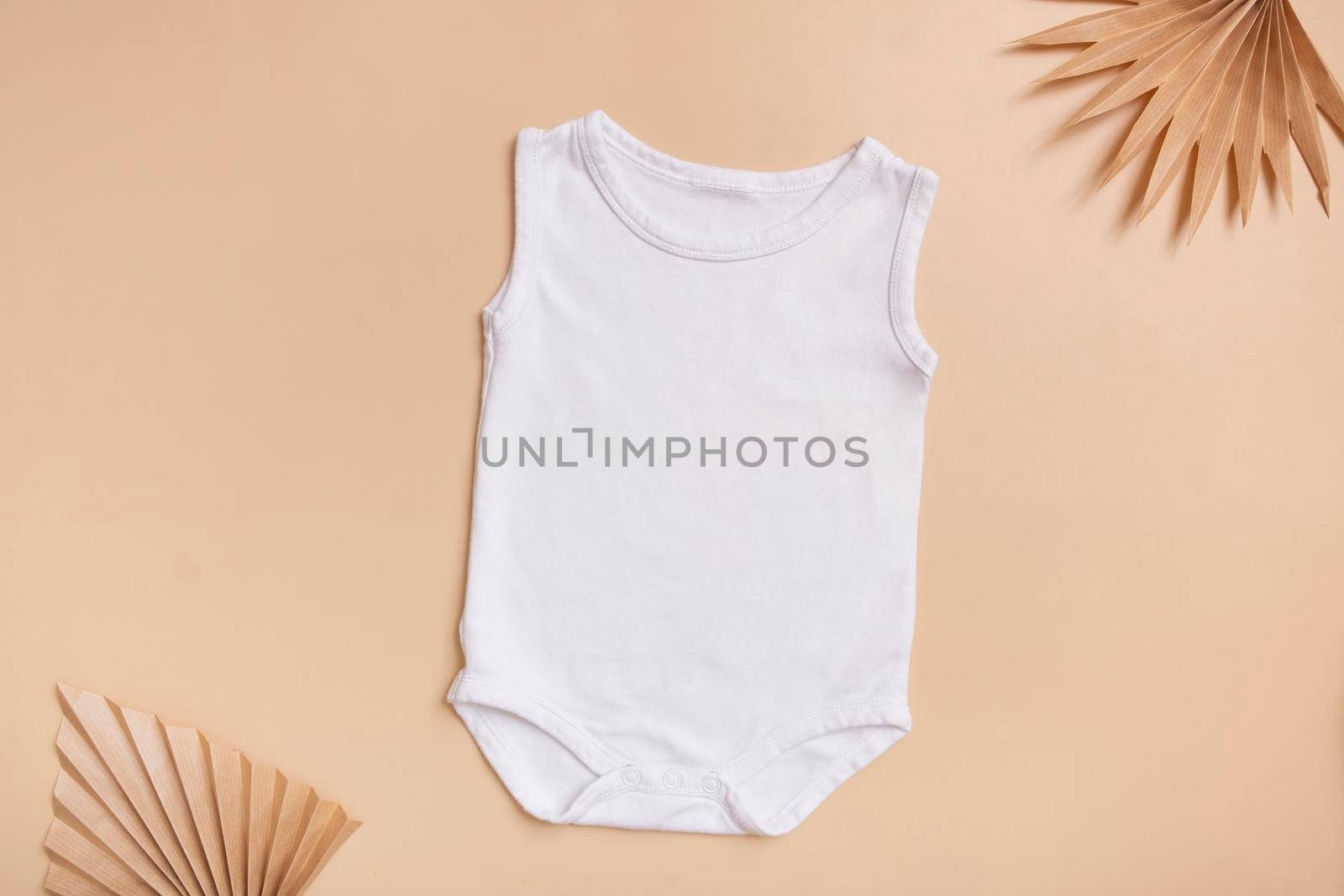 White baby bodysuit mock-up for logo, text or design on beige background with palm leaves top view