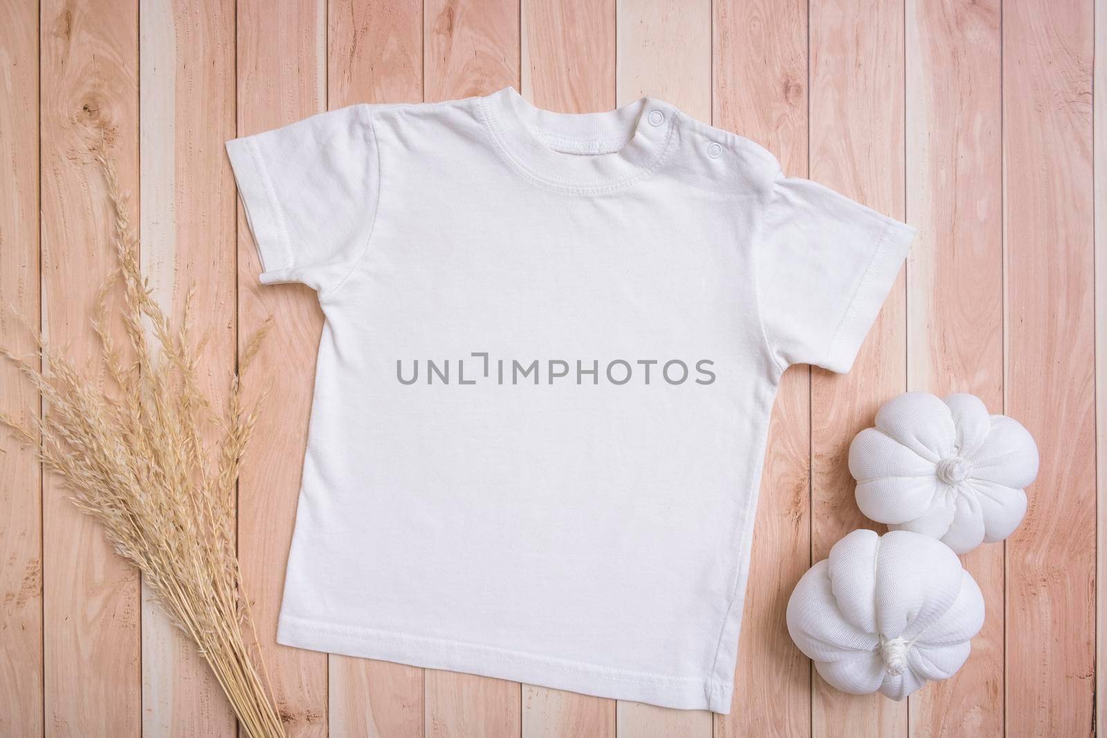 White baby t-shirt top view. Mock-up for logo, text or design on wooden background. Flat lay child clothes with pumpkins by ssvimaliss