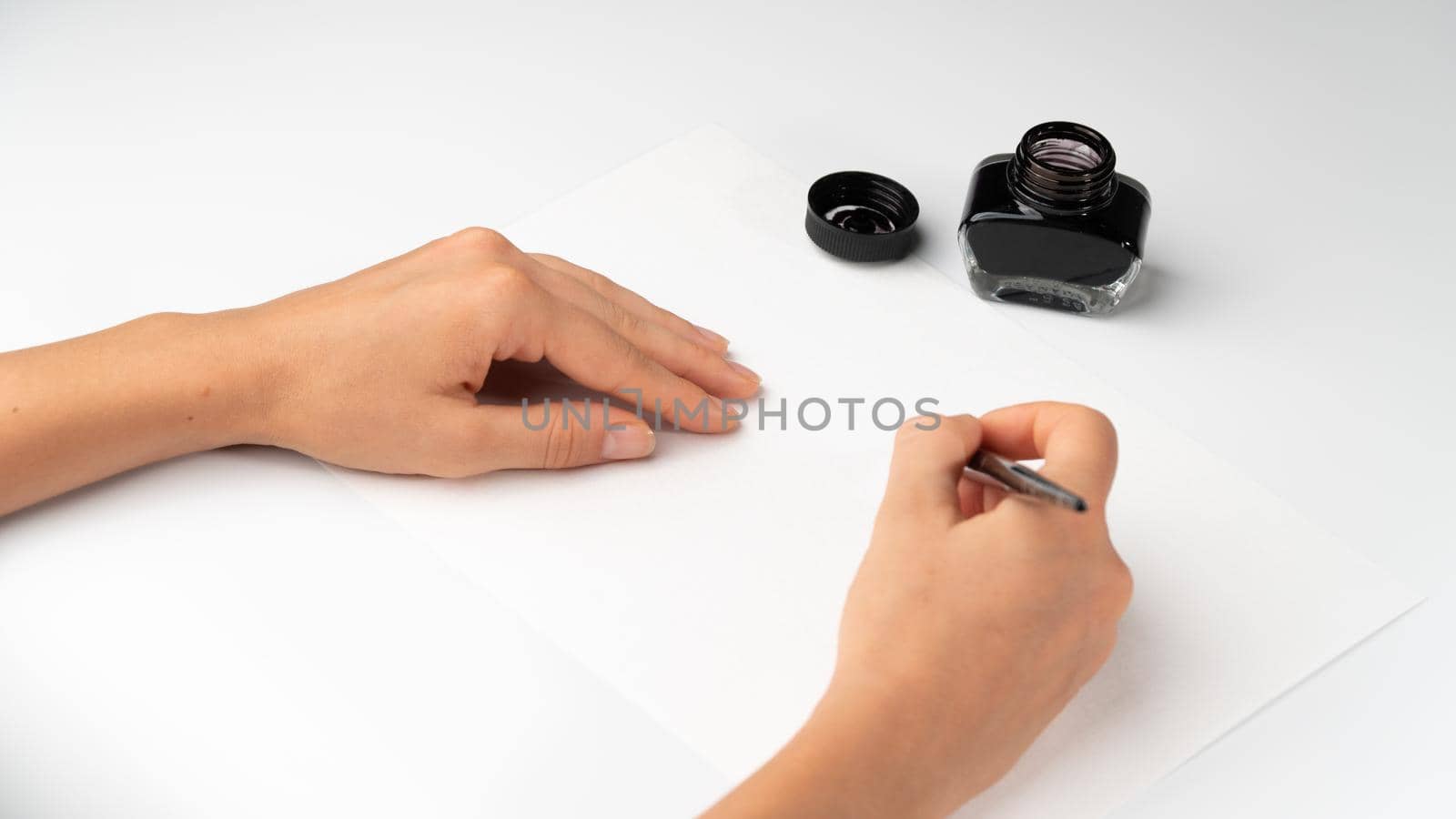 A woman's hands hold a fountain pen on a white background with calligraphy ink