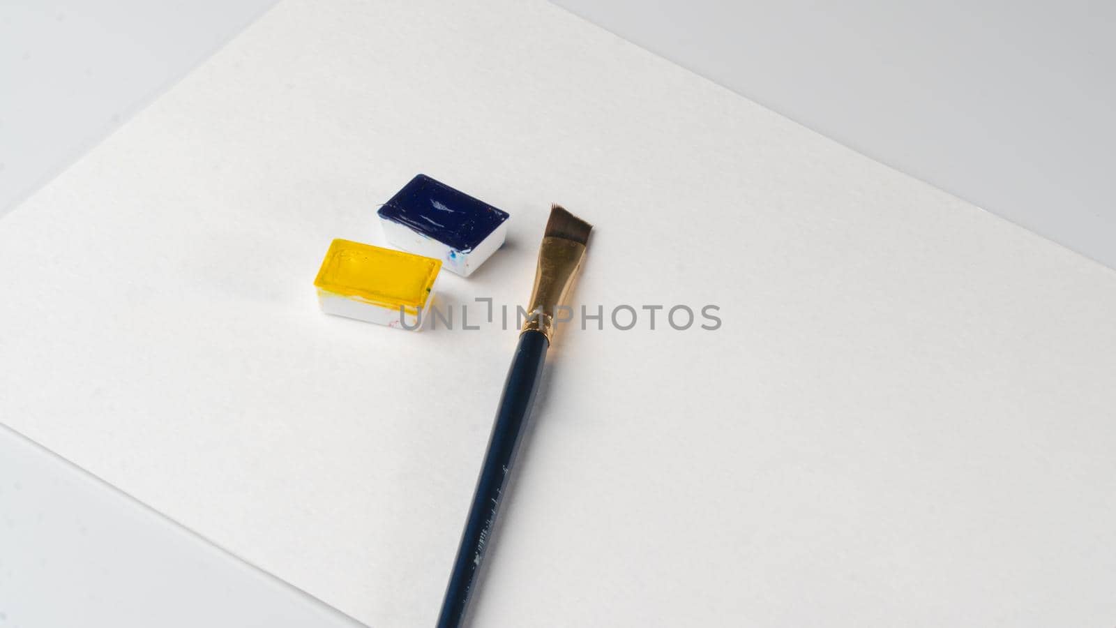 On the sheet are paints and a brush for drawing blue and yellow colors in watercolor ditches. High quality photo