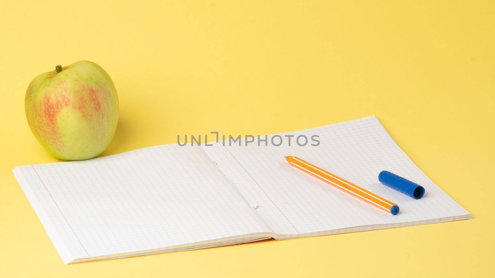 Open checkered notebook with pen and apple on yellow background, study. High quality photo
