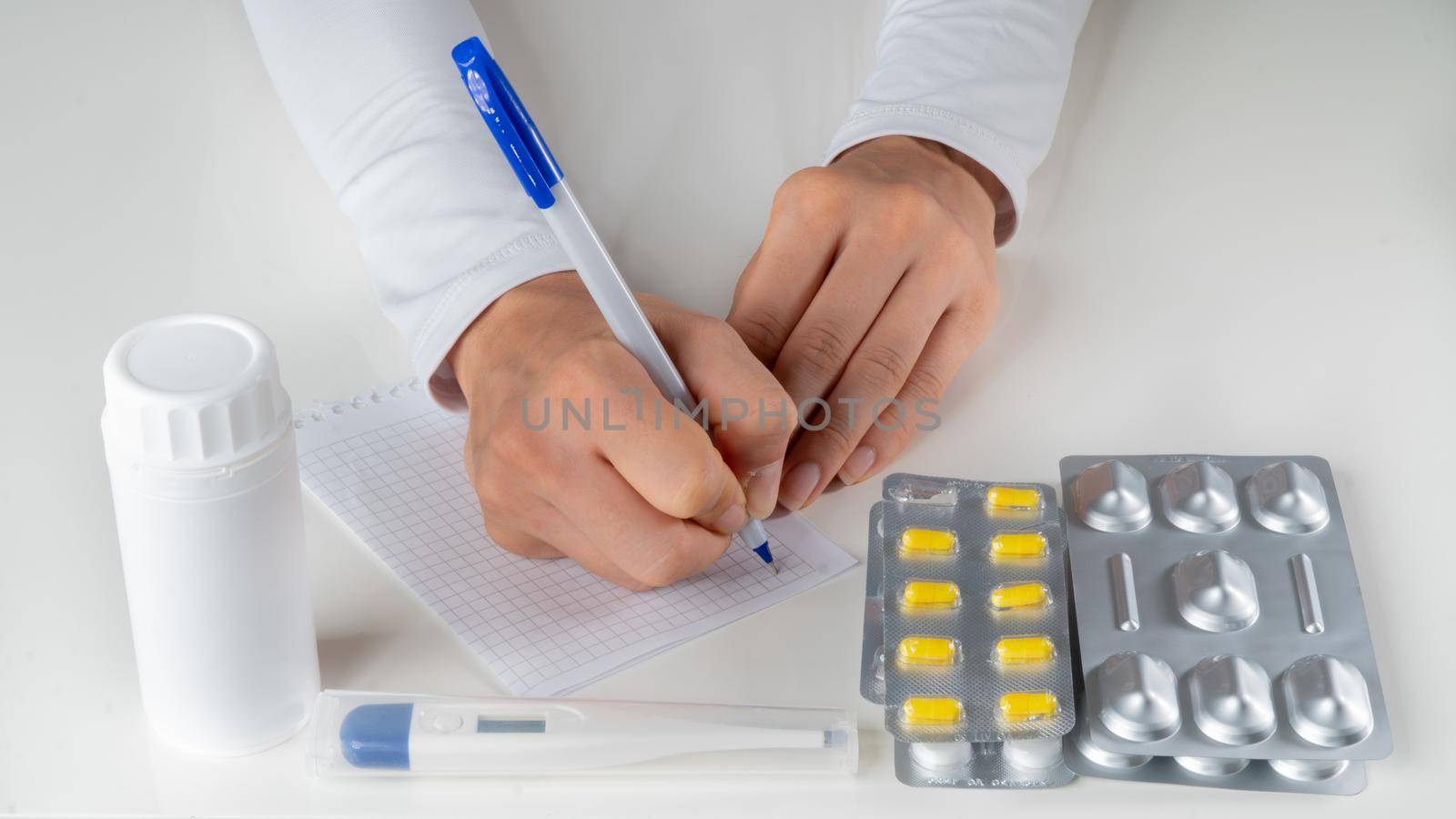 The doctor makes a note on the table with pills and a thermometer. High quality photo