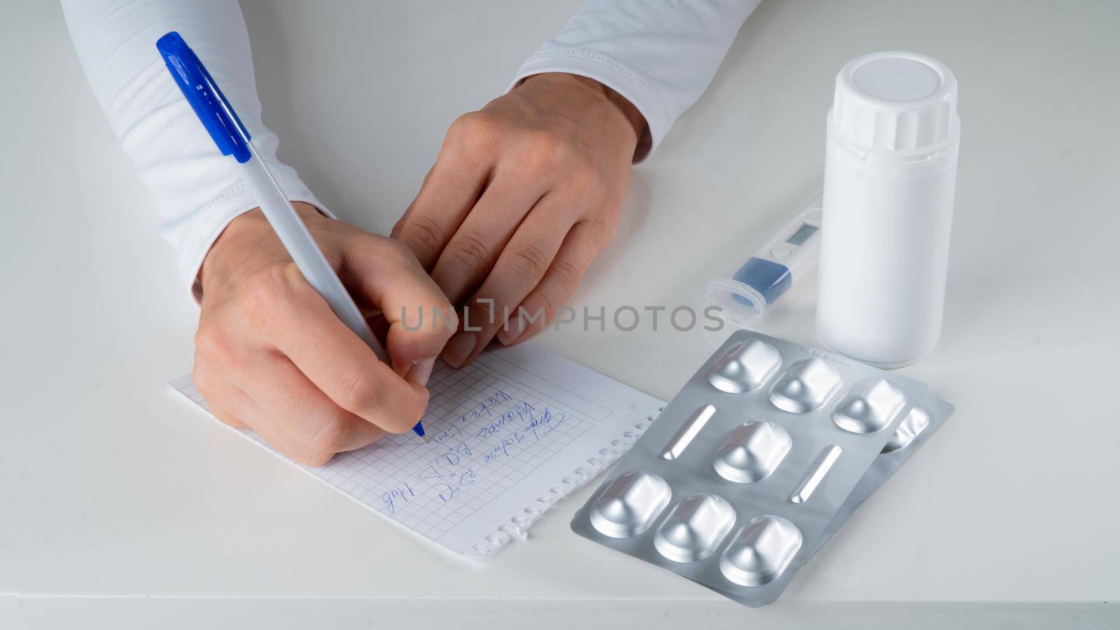 The doctor writes a prescription for the treatment of the hand in a white coat on the background of tablets by voktybre