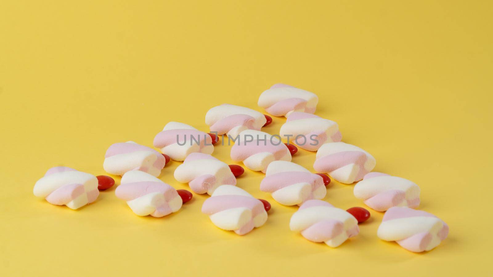 Marshmallows and red candy dragees in the form of a triangle on a yellow background. High quality photo