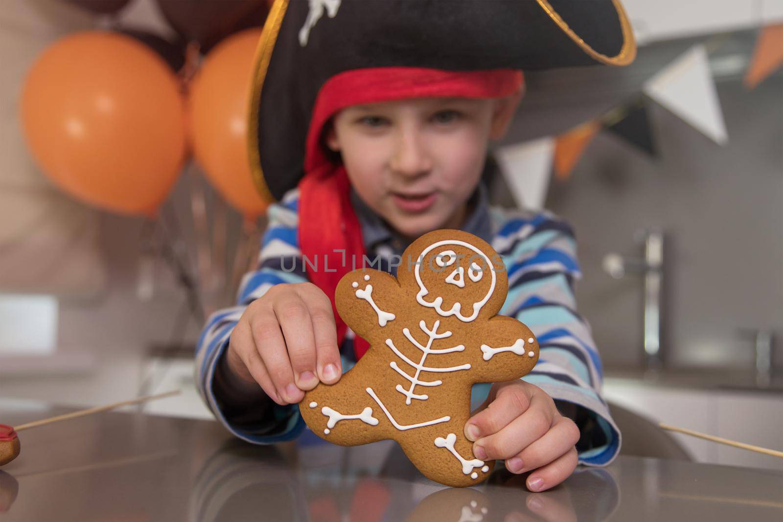 Close-up portrait of a boy dressed as a pirate for Halloween. The child eats homemade gingerbread in the form of a skeleton and shows a cookie close-up. House party concept for the whole family