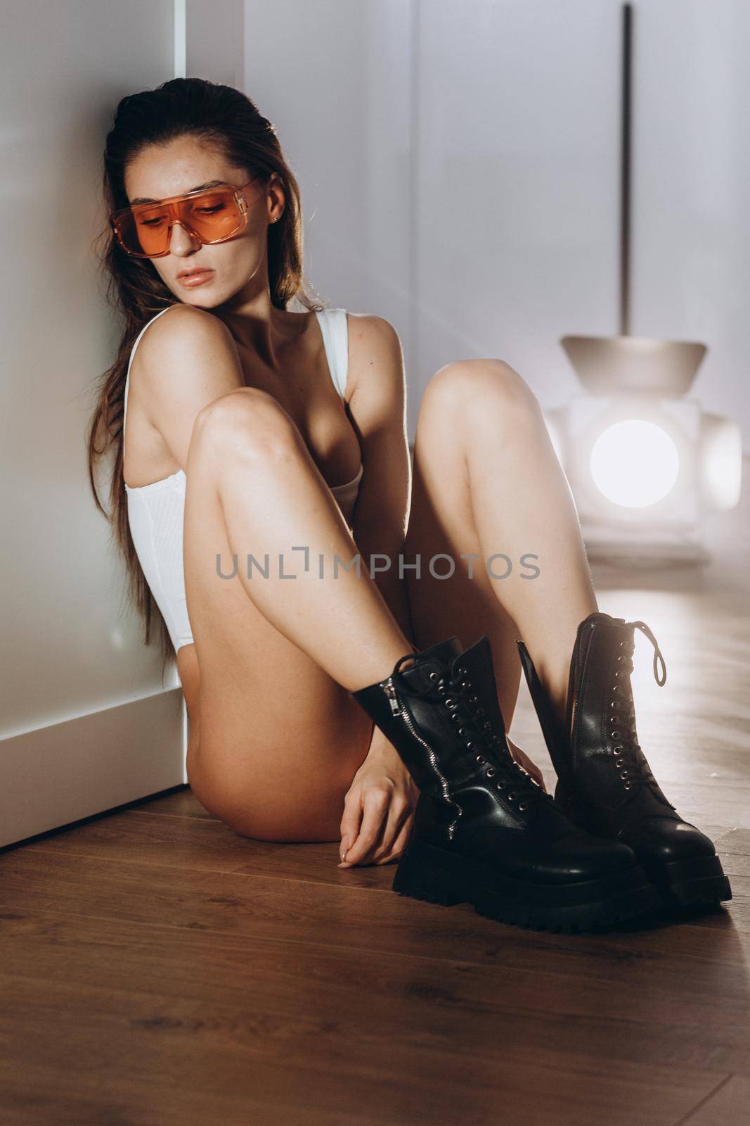 A young beautiful model woman is standing, posing in the kitchen in, white underwear. The girl has long dark hair, full lips and a beautiful face. Tanned, athletic, skinny body in the bodysuit.