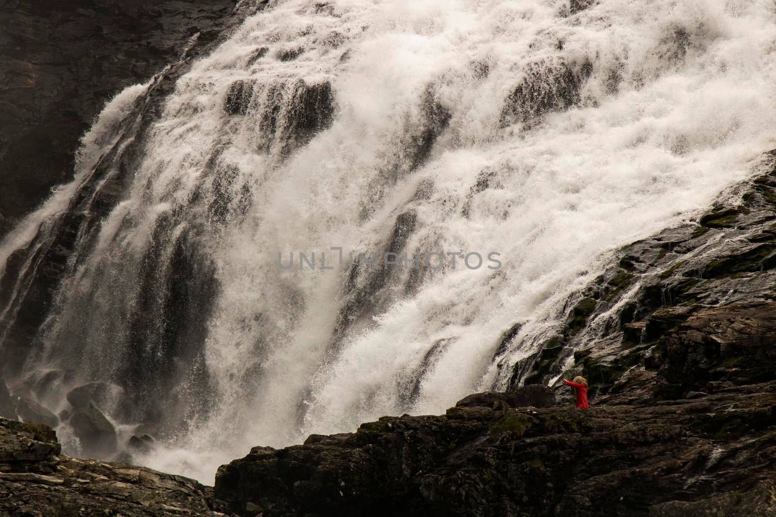 Woman in red dress dancing above Kjosfossen waterfall close to Flam tourist town in Norway