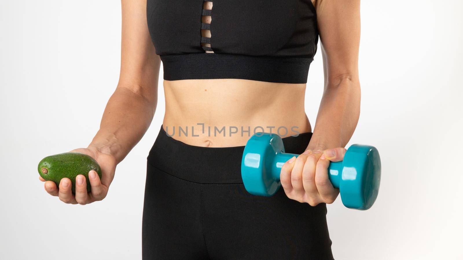 A woman in sportswear holds a dumbbell and avocado in her hands - a healthy diet and sports. High quality photo