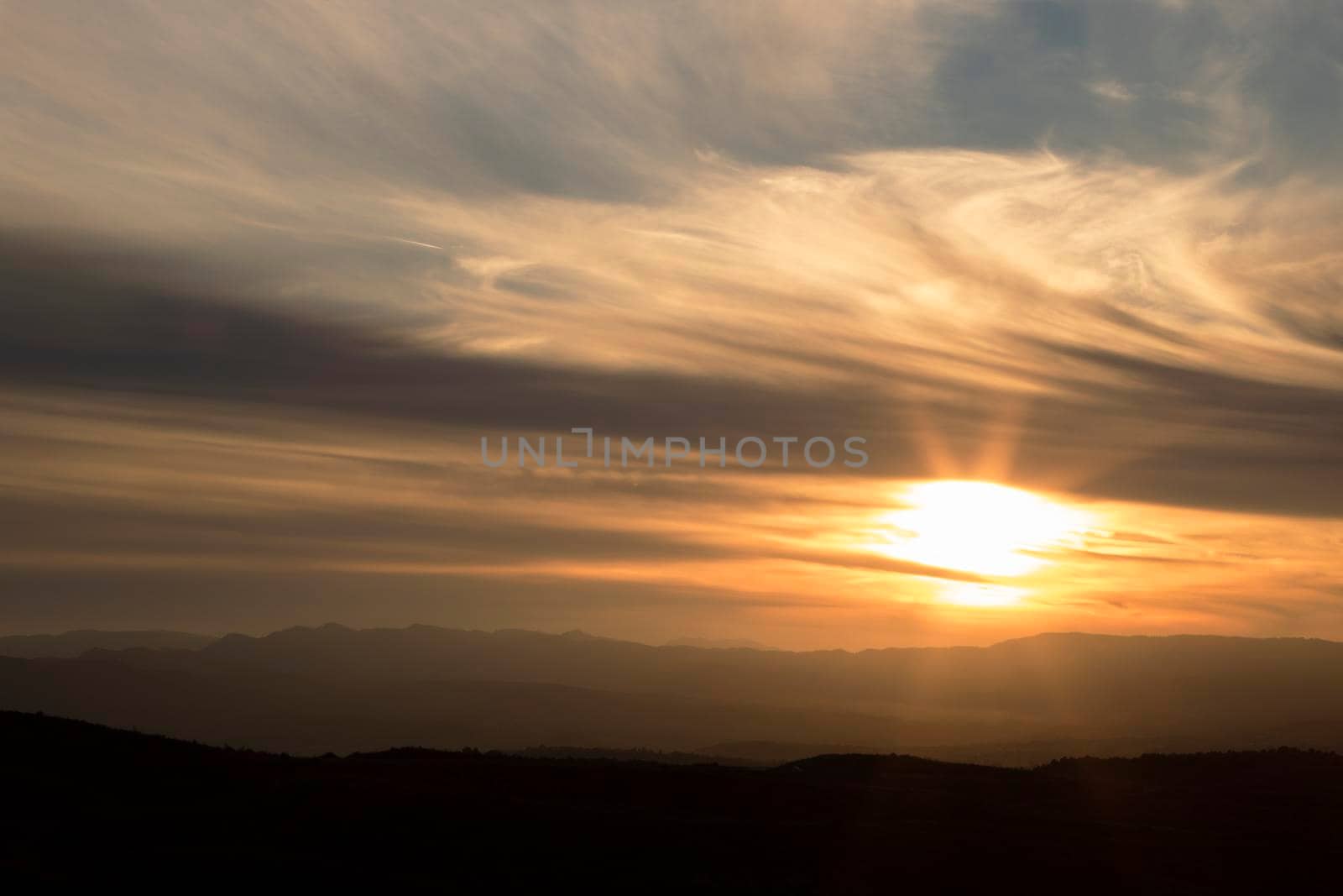 Landscape showing a cloudy and orange sunset over the mountain