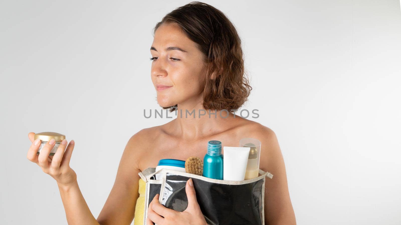 A woman after a shower with a cosmetic bag in her hands - chooses a cream, self-care at home. High quality photo