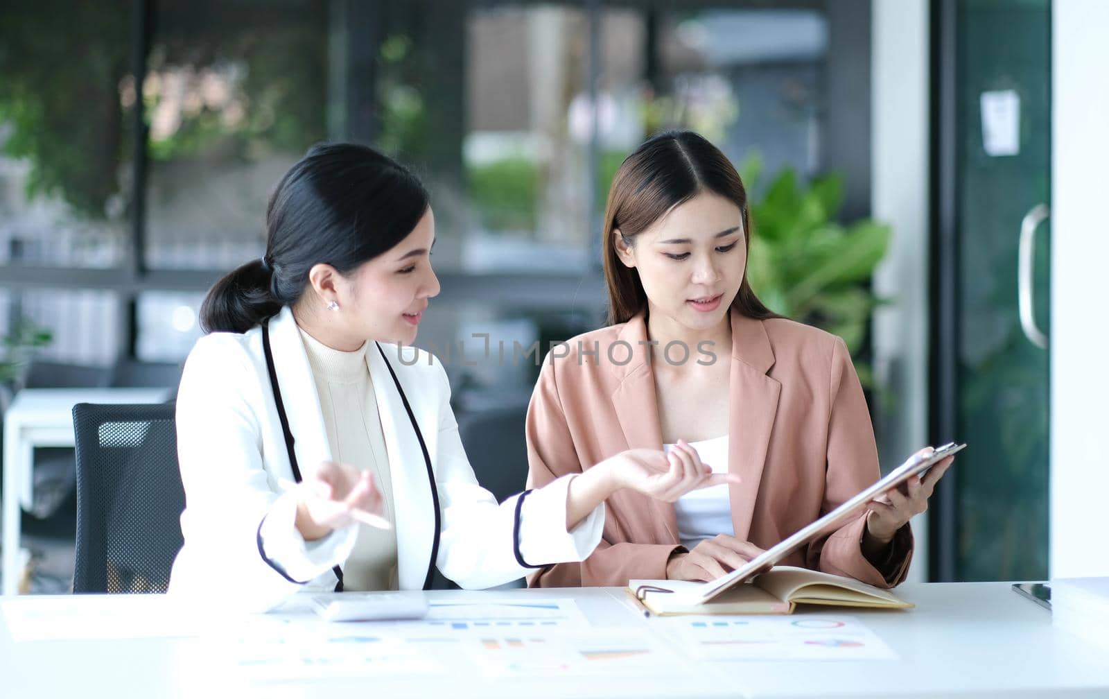 Two young Asian businesswoman discuss investment project working and planning strategy. Business people talking together with laptop computer at office..