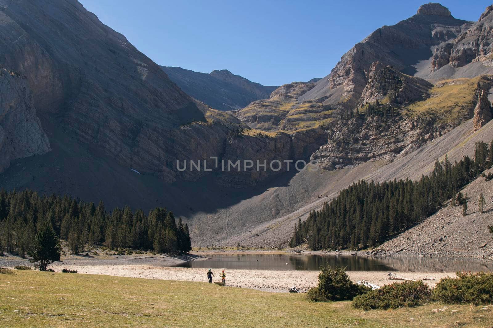 Ibon de Plan lake surrounded by high mountains and some bikers in Pyrenees in Huesca Spain