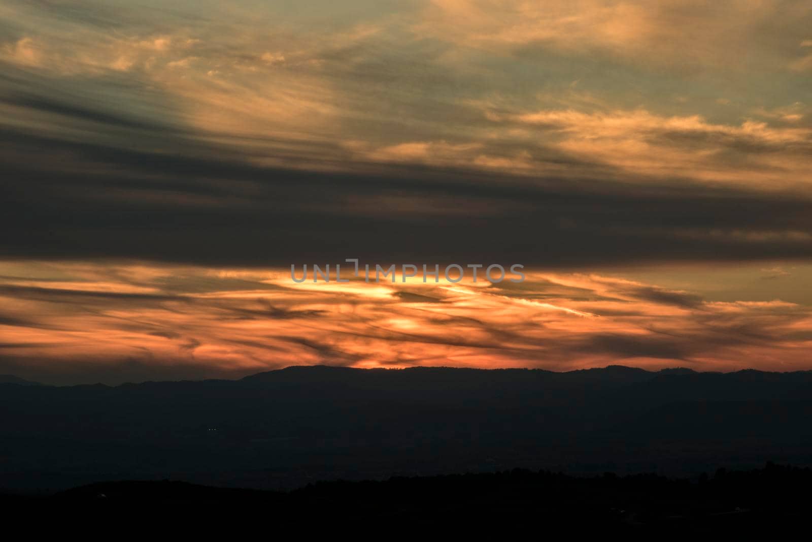 Landscape showing a cloudy and orange sunset over the mountain