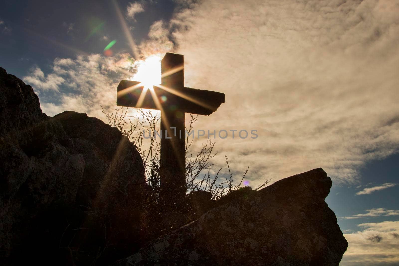Stone christian cross over a mountain and next to the sun