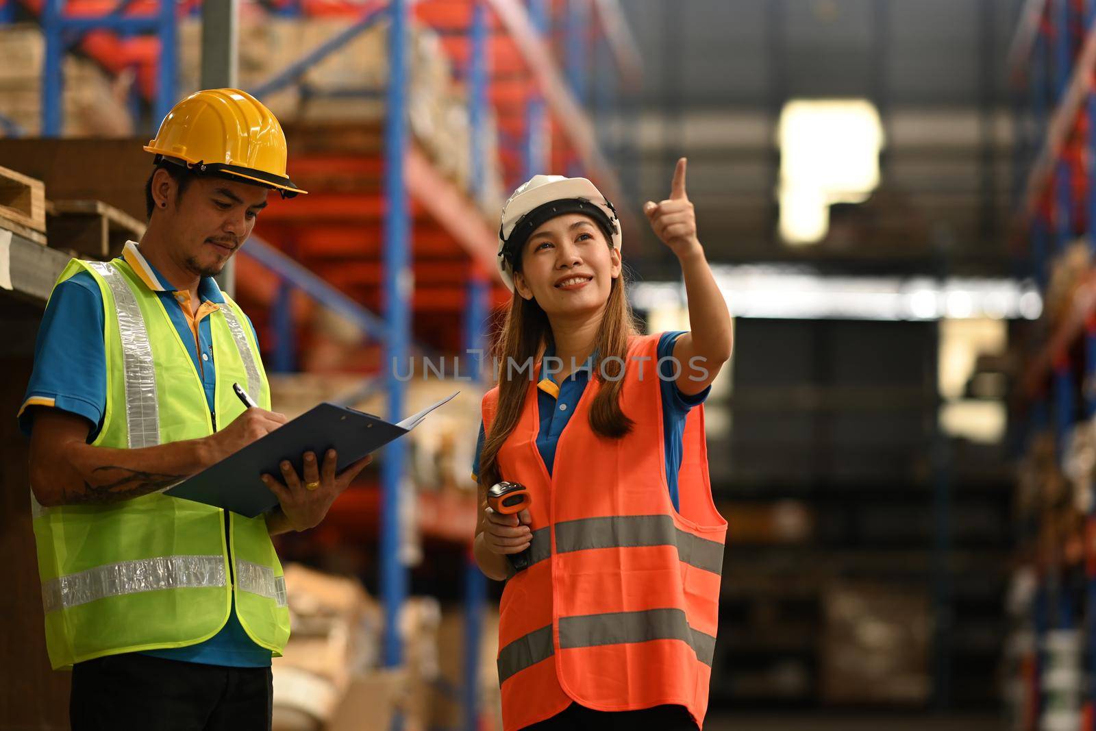 Warehouse workers in hardhats and and vests inspecting stock tick on digital tablet in a large warehouse by prathanchorruangsak