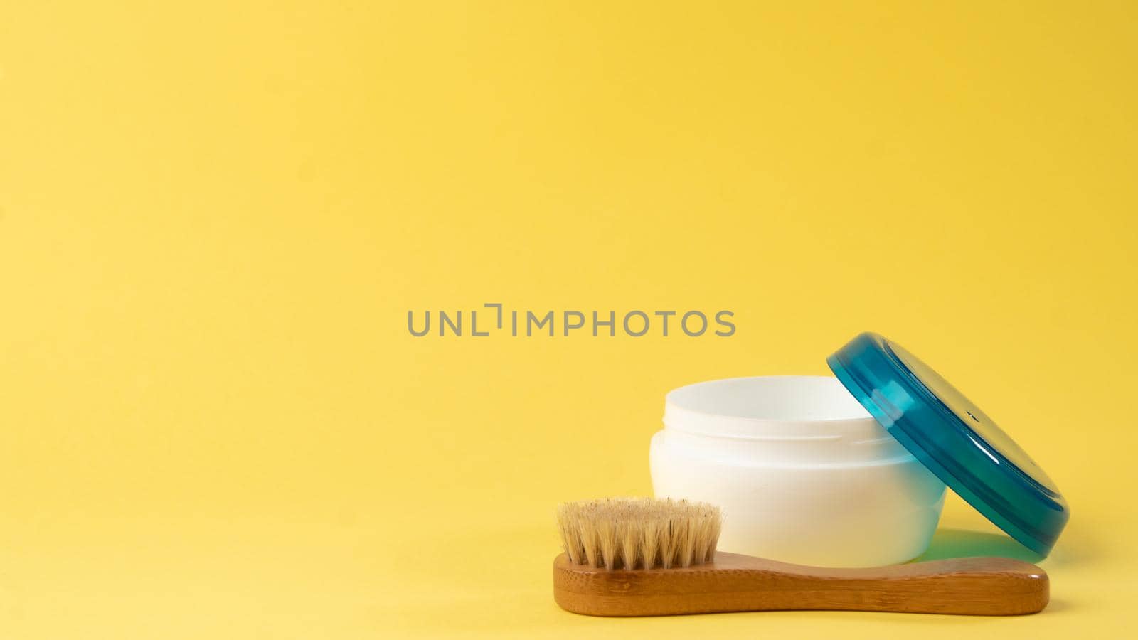 A jar of cream and a massage brush on a yellow background. High quality photo