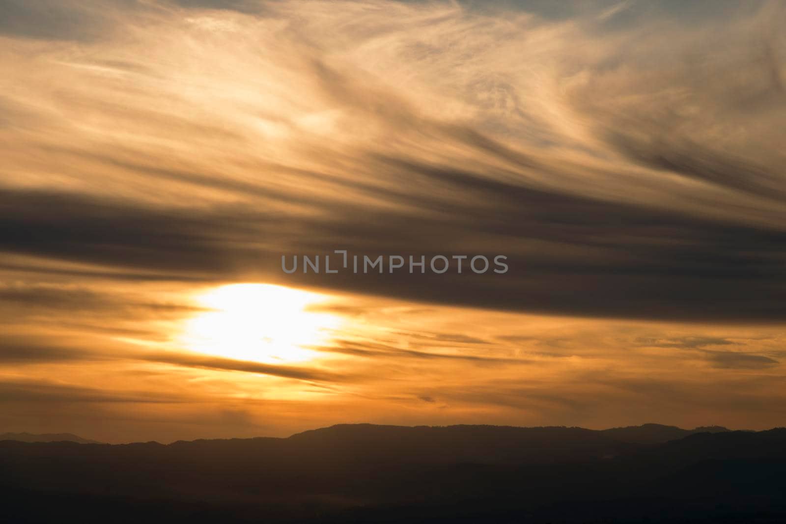 Landscape showing a cloudy and orange sunset over the mountain