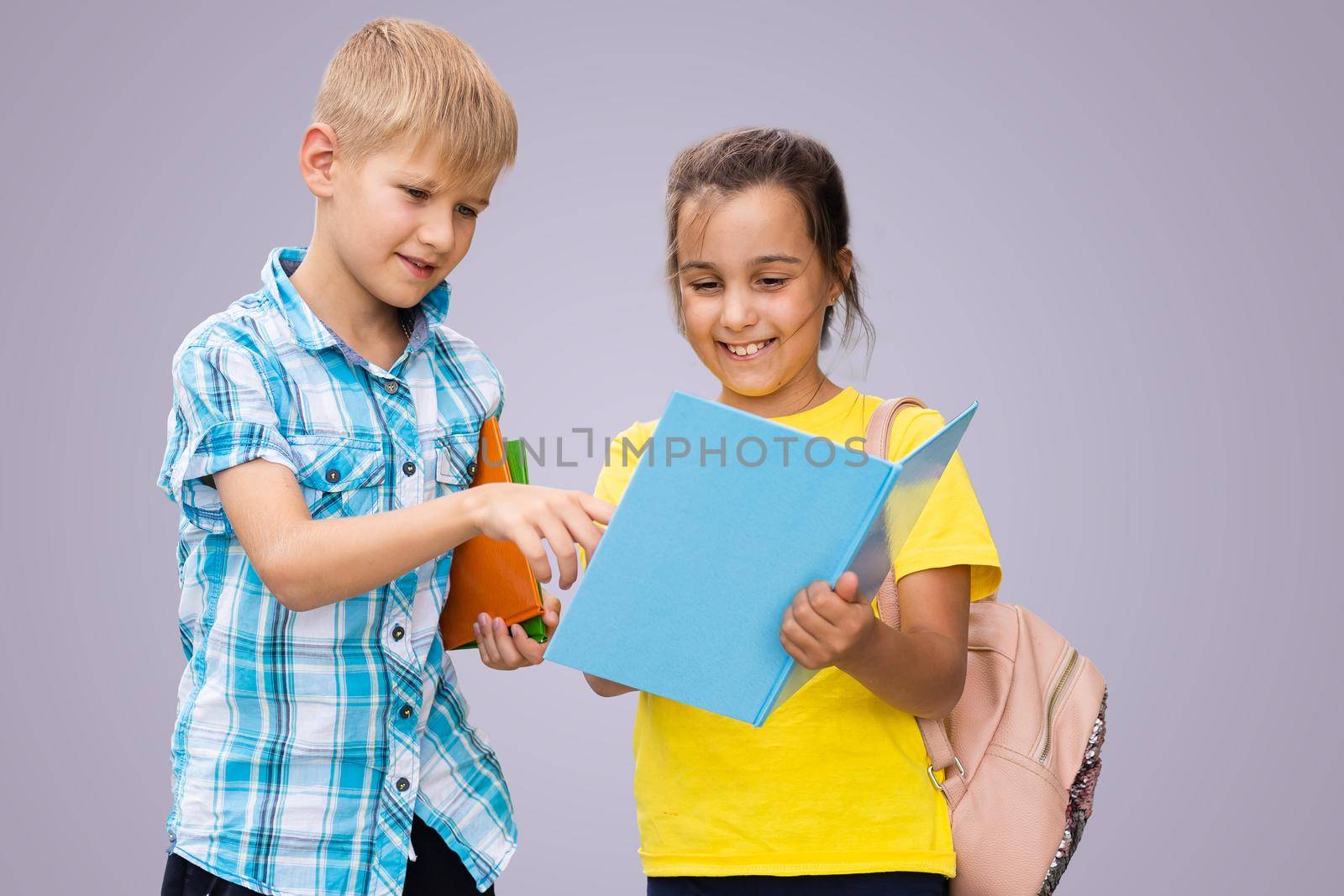 Education Concept. Set portrait of diverse schoolchildren holding stack of academic books and wearing backpack, yellow orange color studio background.