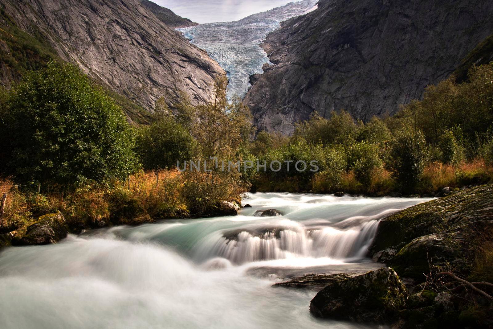 Landscape showing Briksdal glacier in a rocky valley with trees and a river in long exposure picture