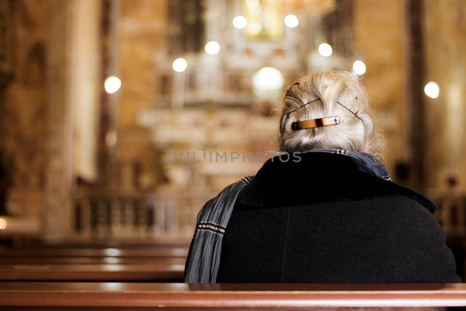 Old woman praying in the church and bokeh effect with the candles in the background