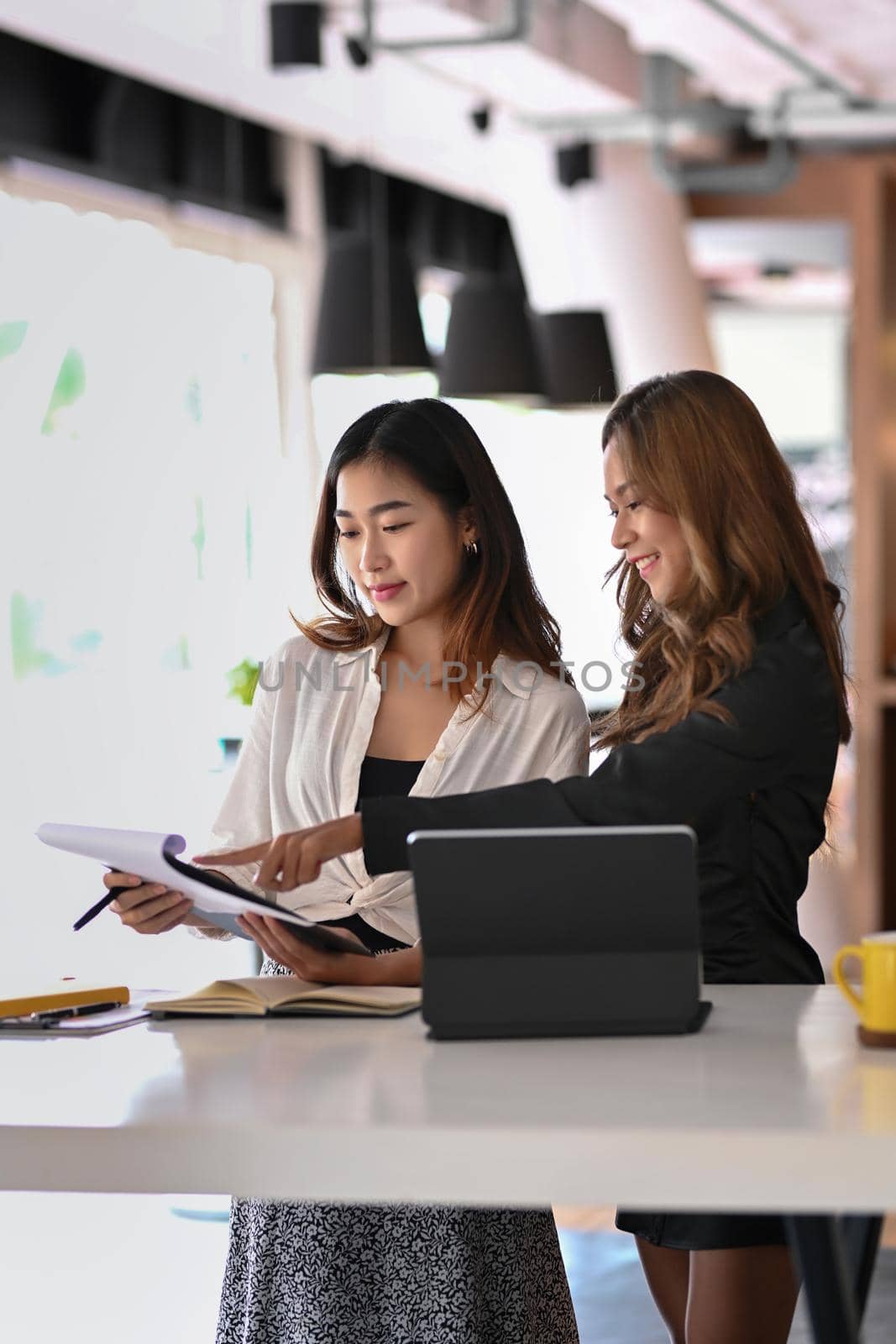 Two young female entrepreneurs working together in modern workplace. by prathanchorruangsak