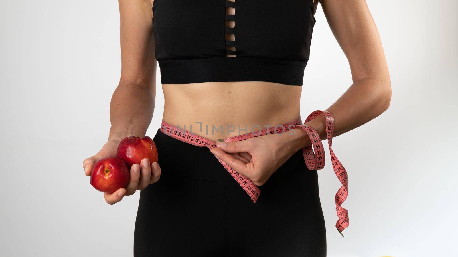 A woman with a slender figure measures her waist with a measuring tape, fruit in her hands. High quality photo