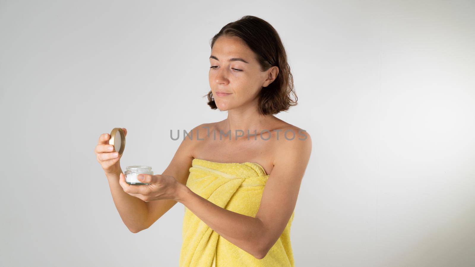 A woman after a shower holds a jar of cream in her hands - skin care of the body and face. High quality photo