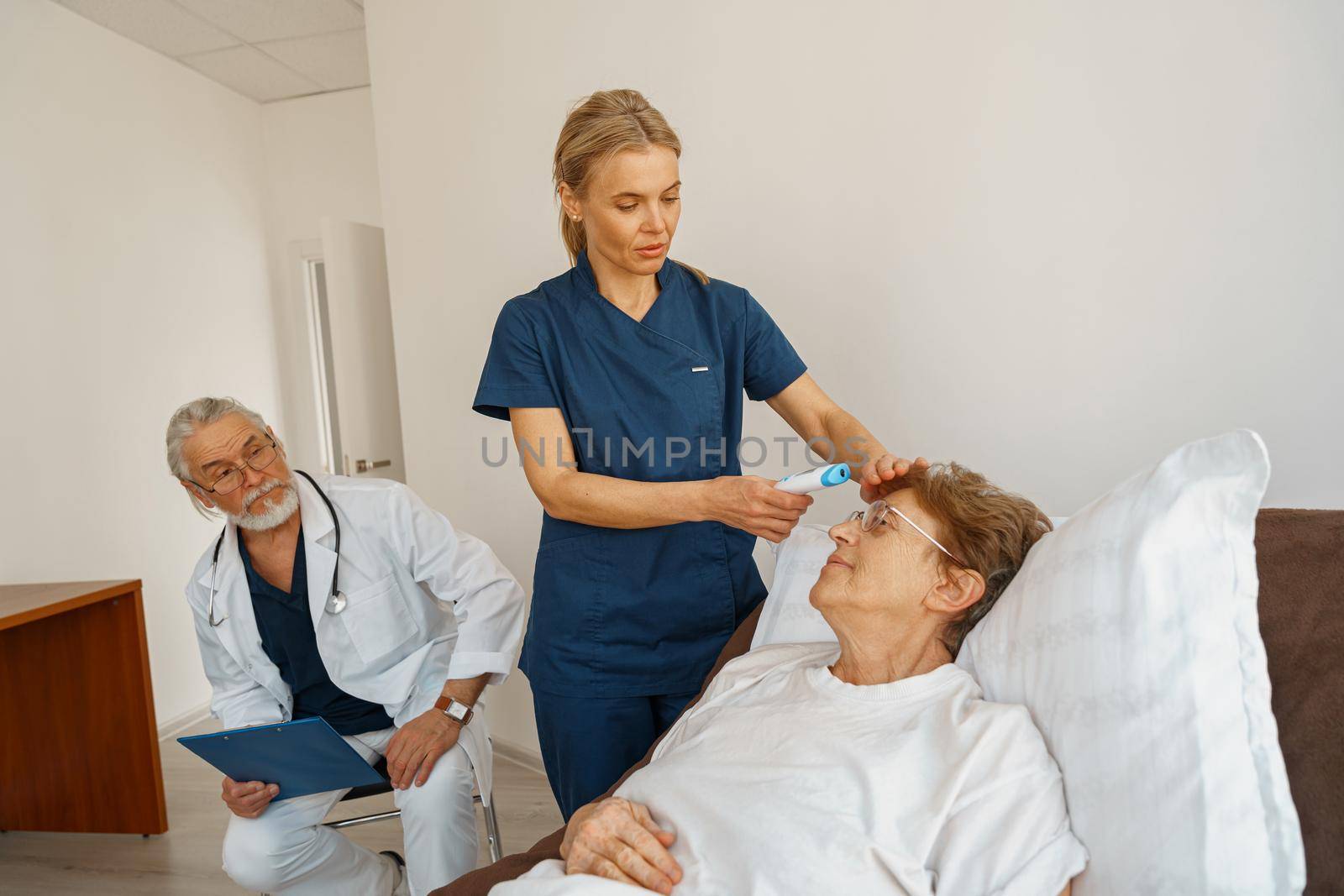 Doctor measures patient's temperature with non-contact thermometer during treatment in hospital ward