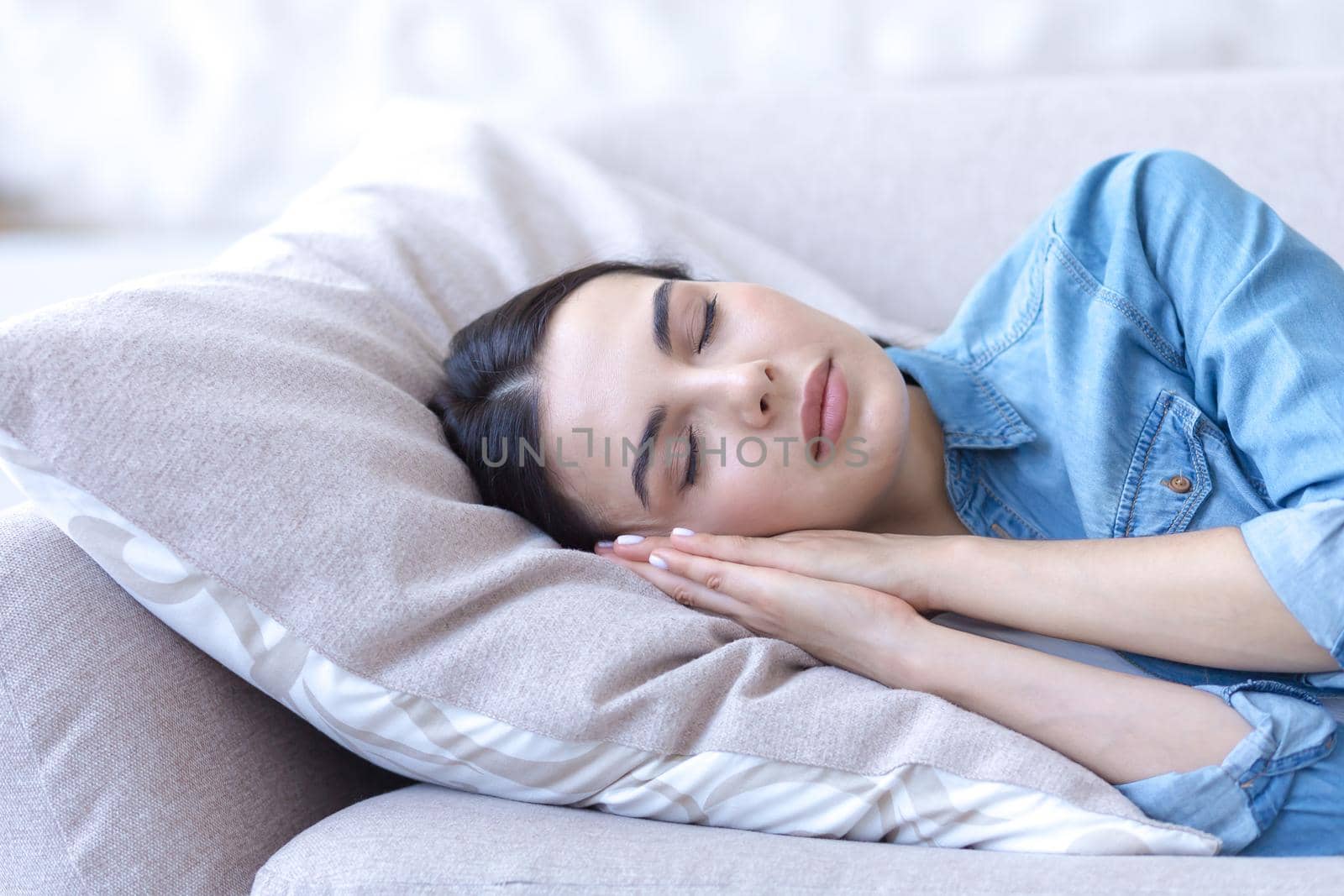 Close-up photo. A beautiful young woman sleeps and rests with closed eyes on a sofa on a pillow, hands folded under her head. Calm, relaxed.