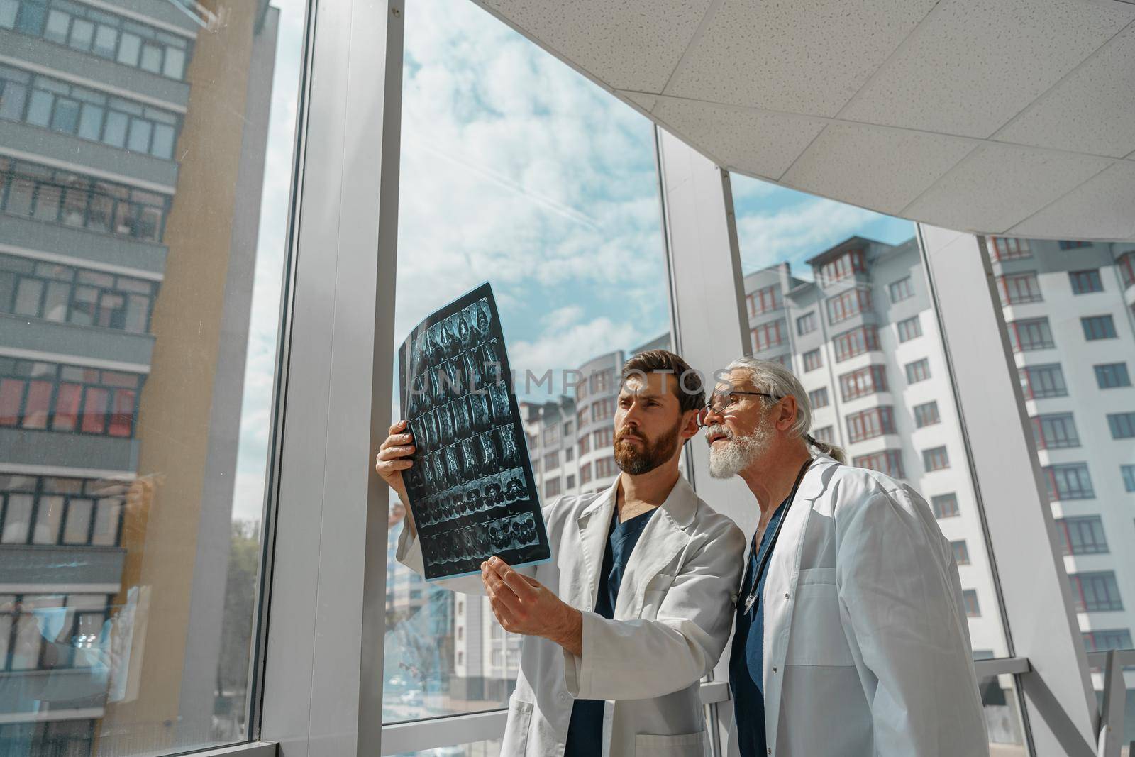 Two doctors in uniform look and discuss an X Ray or MRI scan of the patient spine in clinic