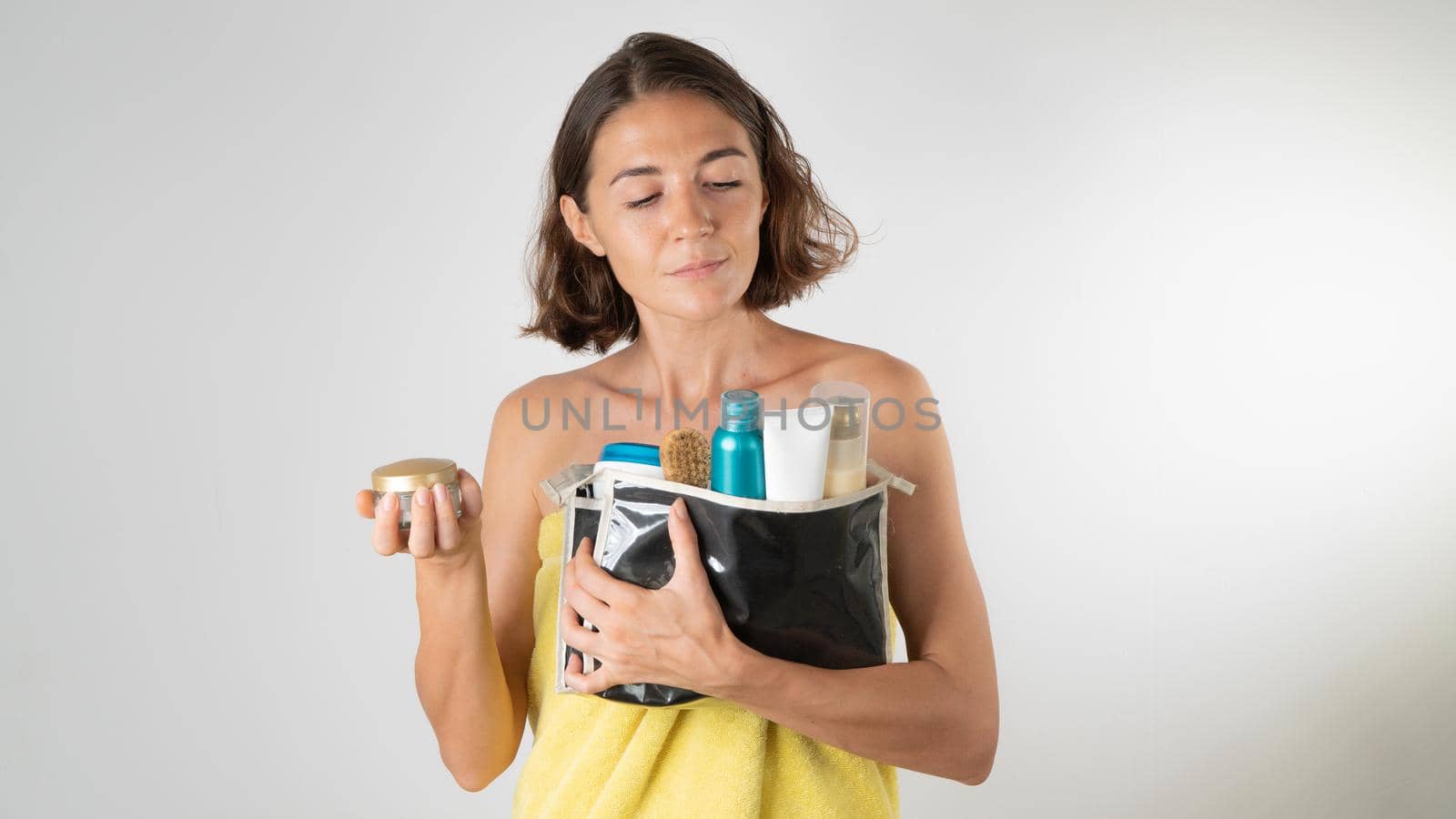 A woman after a shower chooses a cream from a cosmetic bag - self-care. High quality photo