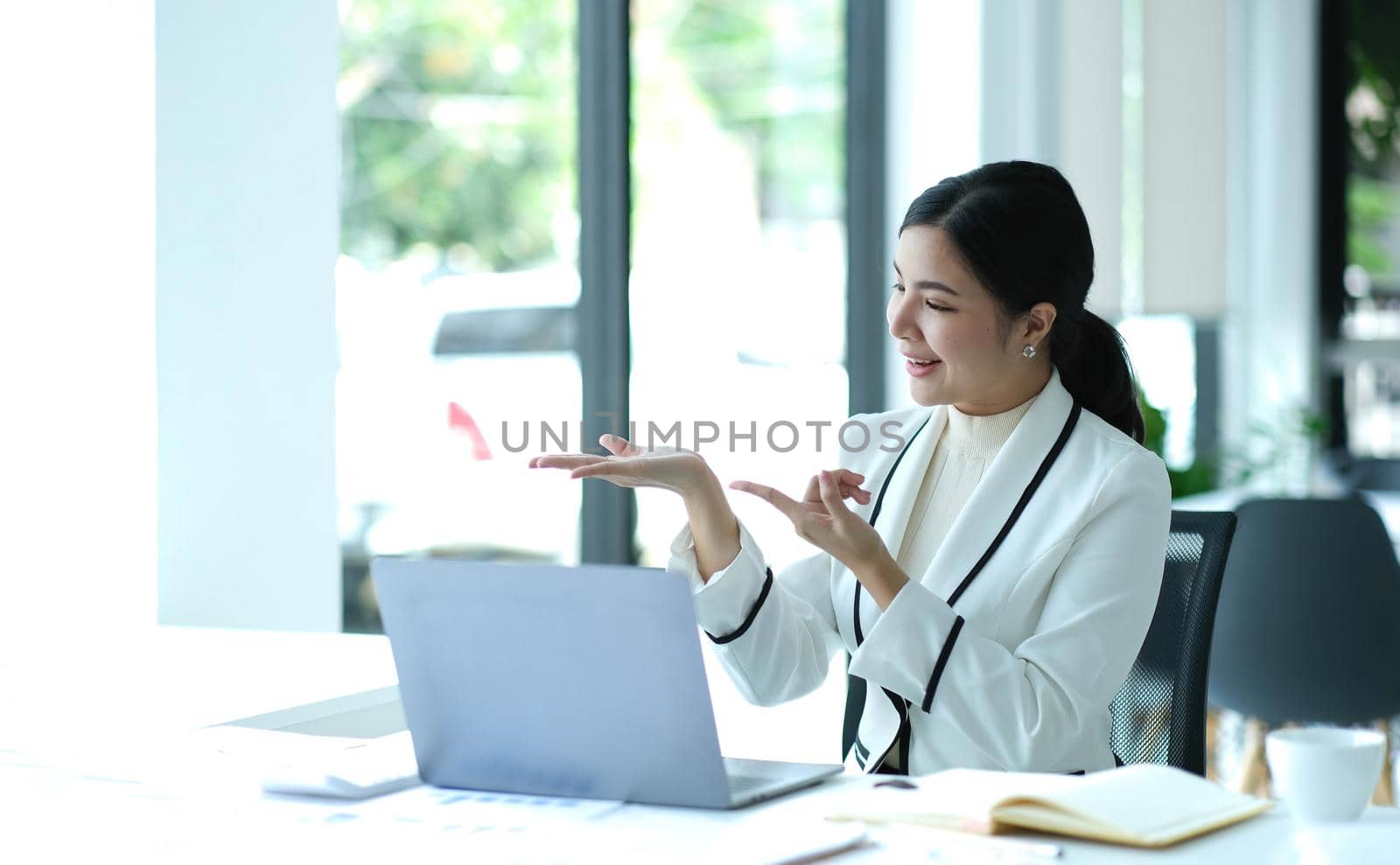 Distant communication. Friendly pretty asian brunette girl, manager, freelancer, sit in the kitchen, talking on video call by laptop with the client or employees, discussing project, smiling.