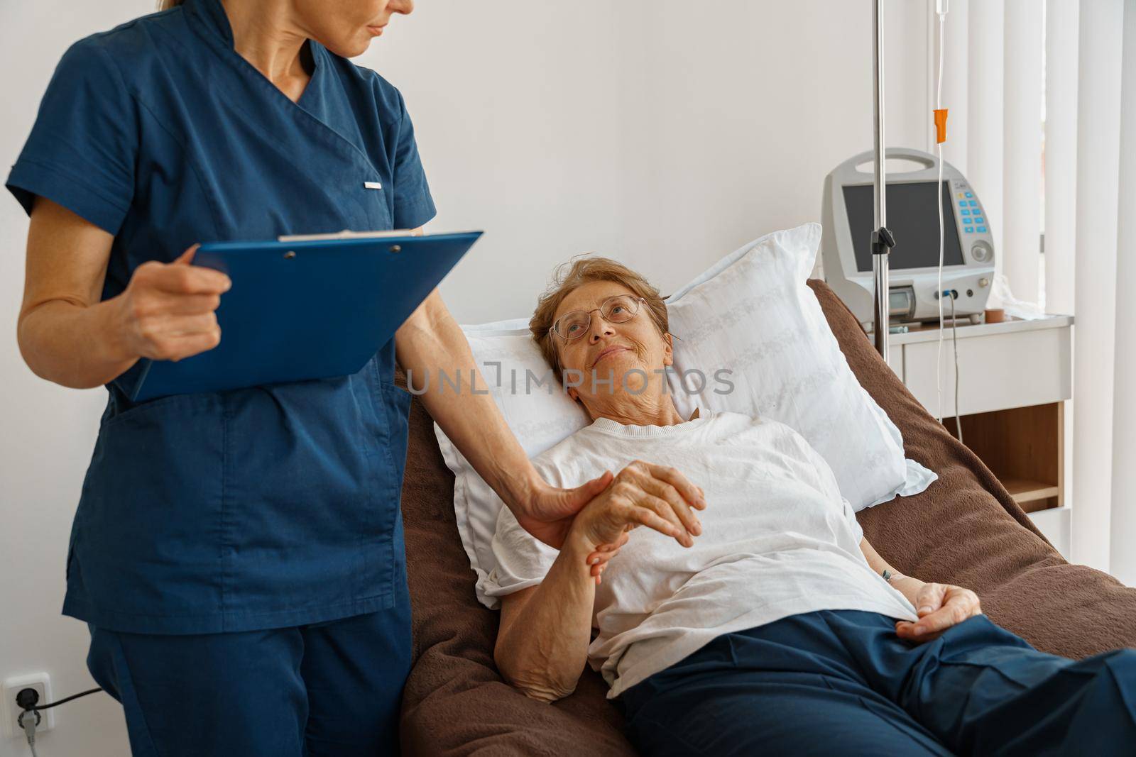 Doctor measures patient's heart rate and makes note in clipboard during treatment in a hospital ward