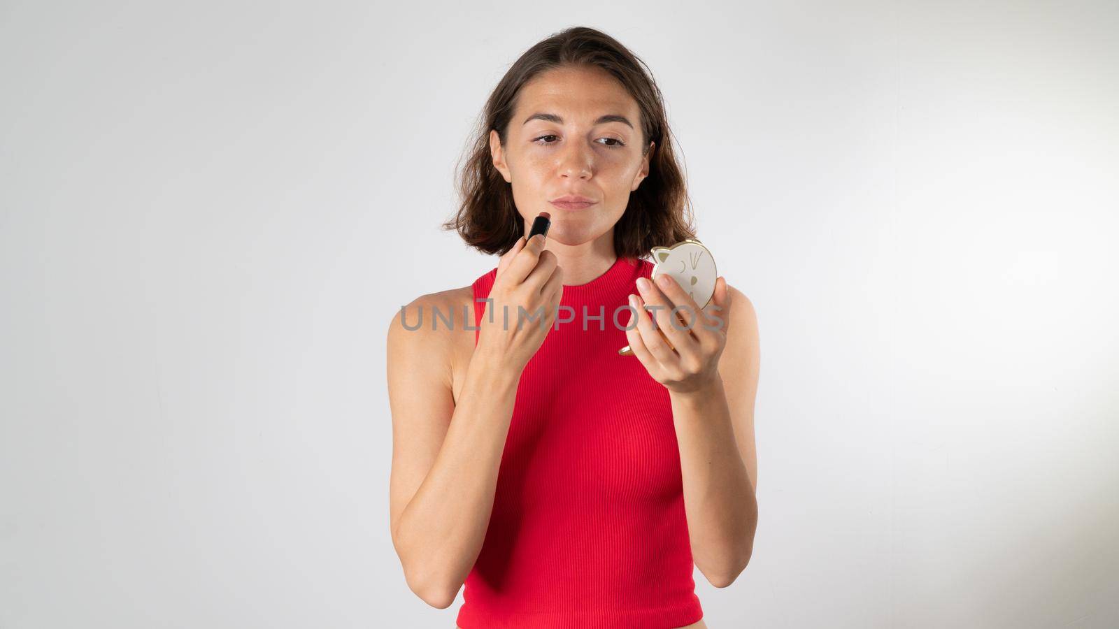 A woman looks into a small mirror and tints her lips with lipstick. High quality photo