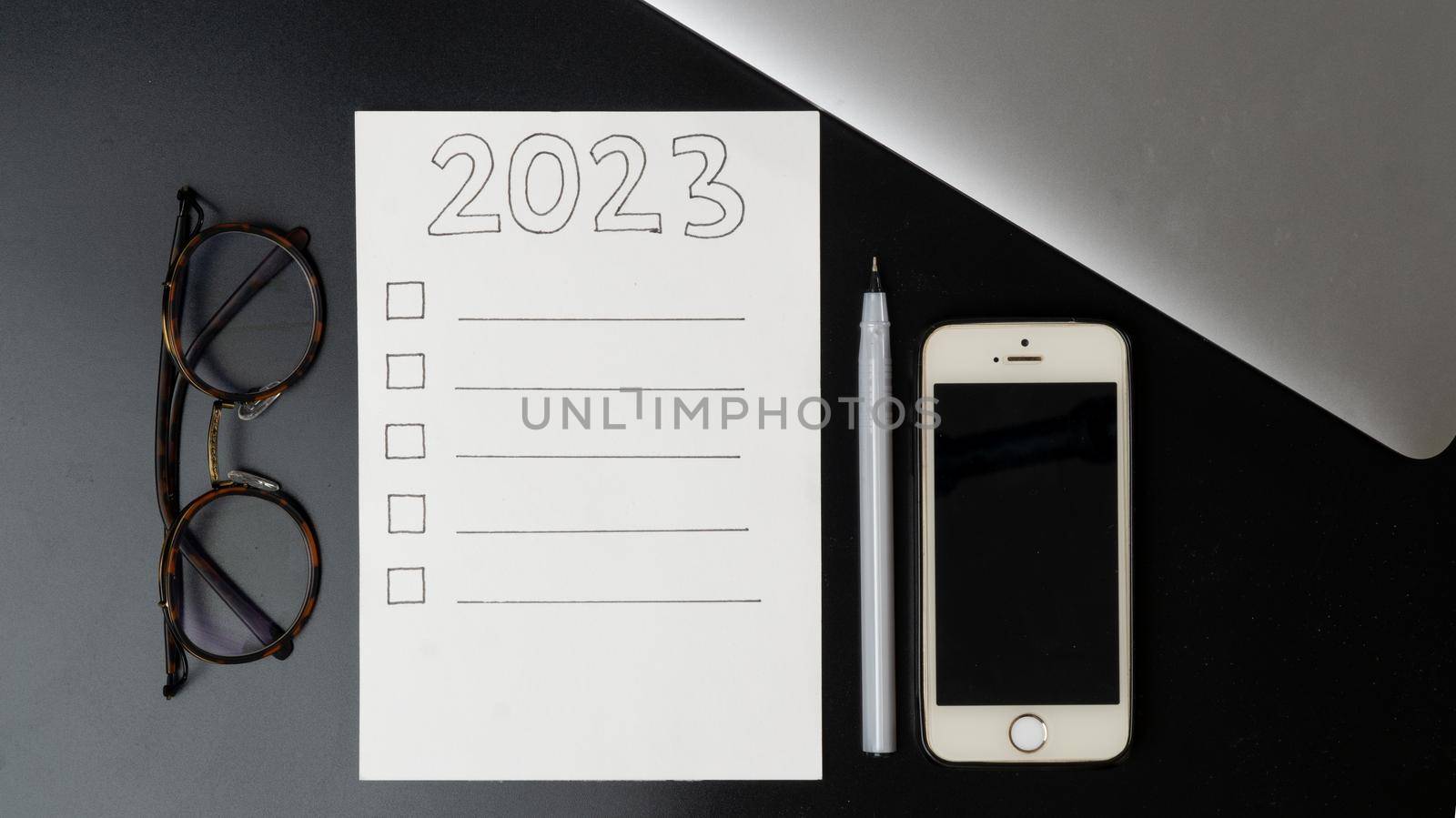 Plan things for the new year 2023, a blank checklist, glasses, phone and laptop on a black background by voktybre