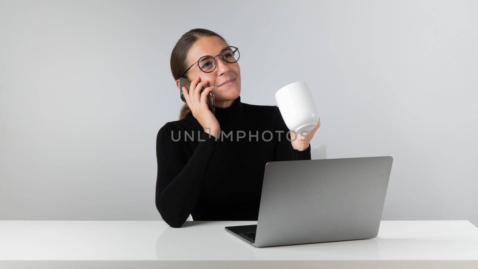 An office worker with a laptop talks on the phone and holds a cup of coffee in her hand. High quality photo