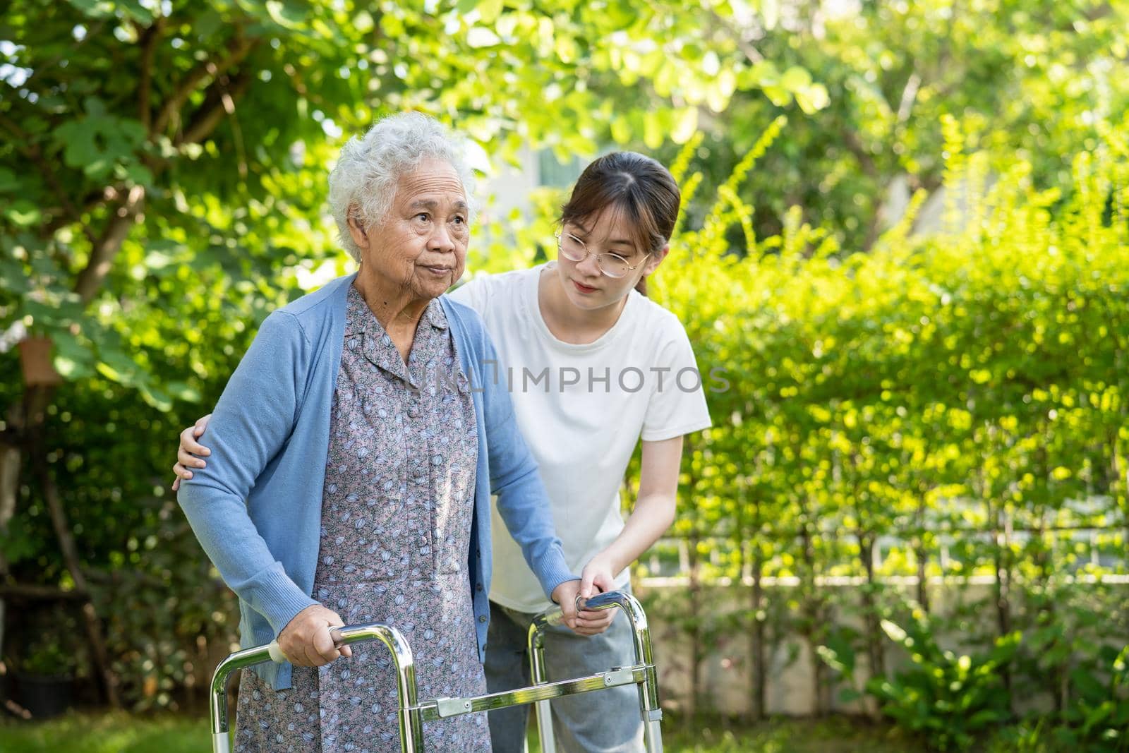 Caregiver help and care Asian senior or elderly old lady woman use walker with strong health while walking at park in happy fresh holiday. by pamai